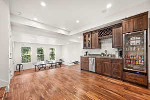 Indoor wet bar with light wood-style floors, dark wood finish cabinets, glass fronted cabinets, and recessed lighting