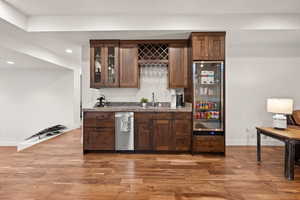 Indoor wet bar with light wood-type flooring, glass fronted cabinets, dark wood finish cabinetry, recessed lighting, and dark countertops