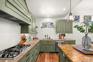 Kitchen with green cabinets, stainless steel appliances, pendant lighting, dark wood-style floors, and light stone countertops