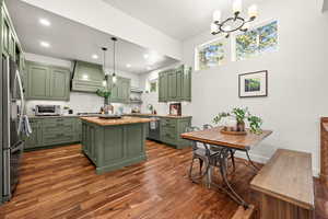 Kitchen featuring green cabinets, a kitchen island, dark wood finished floors, stainless steel appliances, and light stone countertops