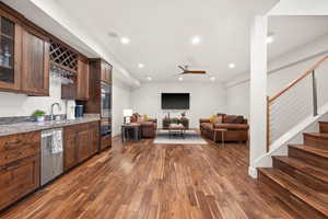 Indoor wet bar with ceiling fan, dark wood-style flooring, dishwasher, glass insert cabinets, and light stone counters