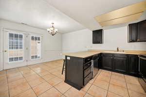 Kitchen with a peninsula, a kitchen bar, light countertops, dark cabinets, and a textured ceiling