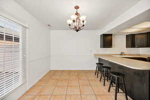 Kitchen featuring light countertops, a breakfast bar, a chandelier, light tile patterned floors, and a peninsula
