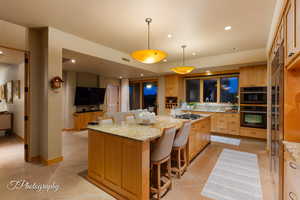 Kitchen with a kitchen breakfast bar, light stone countertops, pendant lighting, and light tile patterned floors