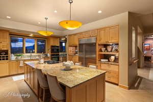 Kitchen with a kitchen bar, light stone counters, stainless steel appliances, pendant lighting, and a kitchen island