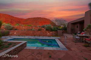 Pool at dusk featuring a mountain view, a patio, outdoor dining space, a fenced backyard, and a pool with connected hot tub