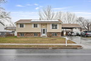 Split foyer home featuring a front yard, concrete driveway, brick siding, roof mounted solar panels, and an attached carport