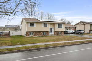 Raised ranch featuring roof mounted solar panels, brick siding, driveway, a gate, and a carport