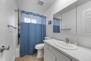 Bathroom with vanity, shower / bathtub combination with curtain, light tile patterned floors, and a textured ceiling