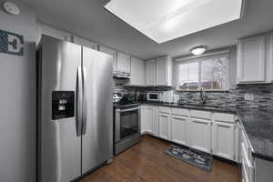 Kitchen featuring stainless steel appliances, white cabinetry, dark stone countertops, a textured ceiling, and dark wood-style floors