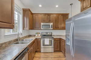 Kitchen featuring stainless steel appliances, decorative light fixtures, light wood-style floors, and wood finish cabinetry