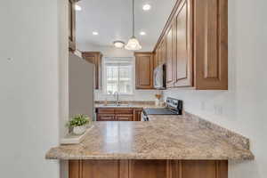Kitchen featuring stainless steel appliances, wood finish cabinets, hanging light fixtures, and light stone counters