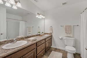 Full bath with double vanity, a shower with shower curtain, and dark stone finish floors