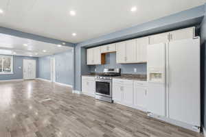 Kitchen with white refrigerator with ice dispenser, stainless steel gas range, white cabinetry, recessed lighting, and open floor plan