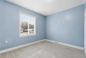 Carpeted empty room featuring a textured ceiling and baseboards
