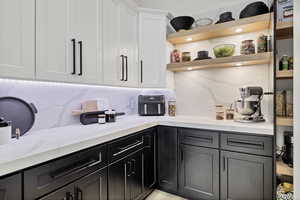 Kitchen with open shelves, two tone cabinetry, tasteful backsplash, and light stone counters