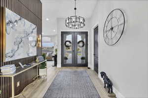 Entrance foyer featuring french doors, light wood-type flooring, and a chandelier