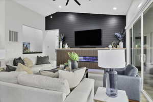 Living room with an accent wall, vaulted ceiling, wood walls, and ceiling fan