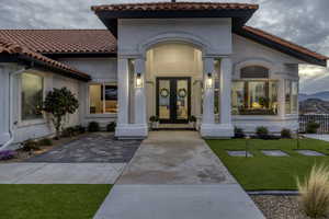 Property entrance with french doors, a lawn, a tile roof, and stucco siding