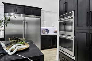 Kitchen with stainless steel appliances, two tone cabinetry, light stone counters, and light wood-style flooring