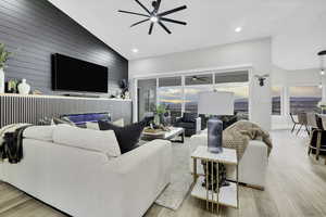 Living area with a ceiling fan, vaulted ceiling, light wood-type flooring, wooden walls, and an accent wall