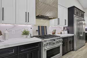 Dual tone kitchen with dual tone cabinets, stainless steel appliances, light stone counters, light wood-type flooring, and tasteful backsplash