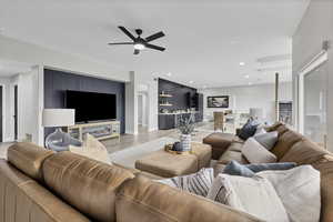 Living room with an accent wall, a ceiling fan, wood finished floors, and recessed lighting