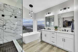 Bathroom featuring a marble finish shower, double vanity, a soaking tub, a spacious closet, and wood tiled floors