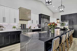 Dual tone kitchen featuring two tone color scheme, a kitchen bar, a large island with sink, light wood finished floors, and vaulted ceiling