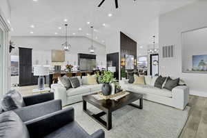 Living room featuring light wood finished floors, ceiling fan, suspended lighting, and lofted ceiling