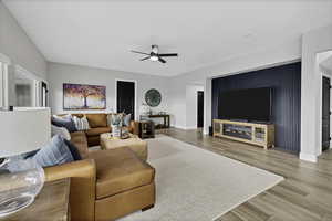 Living room with a ceiling fan, light wood-type flooring, and an accent wall