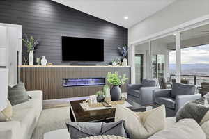 Living room featuring wood finished floors, lofted ceiling, a glass covered fireplace, wooden walls, and recessed lighting