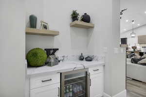 Bar area featuring open shelves, light stone counters, wine cooler, white cabinetry, and lofted ceiling