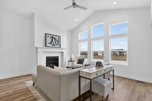 Living area with a high ceiling, light wood-style floors, a ceiling fan, a glass covered fireplace, and recessed lighting