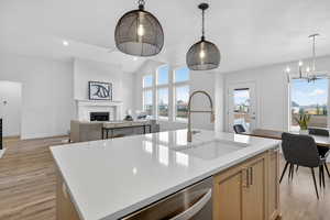 Kitchen featuring open floor plan, vaulted ceiling, light wood-style floors, a center island with sink, and stainless steel dishwasher