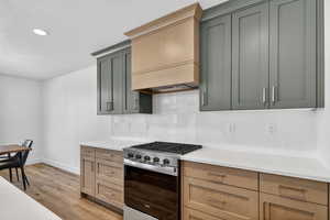 Kitchen featuring stainless steel gas range oven, tasteful backsplash, light wood-type flooring, a textured ceiling, and light stone counters