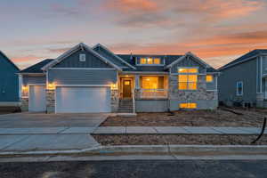 Craftsman inspired home featuring board and batten siding, stone siding, an attached garage, covered porch, and driveway