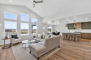 Living room featuring ceiling fan, light wood-type flooring, hanging lights, and lofted ceiling