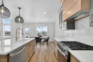 Kitchen with stainless steel appliances, light wood-style flooring, light stone counters, decorative backsplash, and hanging lights