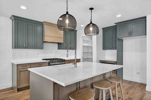 Kitchen with a breakfast bar area, light stone counters, a center island with sink, light wood finished floors, and pendant lighting