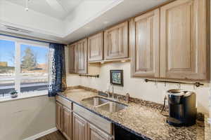 Kitchen with light stone counters, light wood finish cabinetry, ceiling fan, dark wood finished floors, and black dishwasher