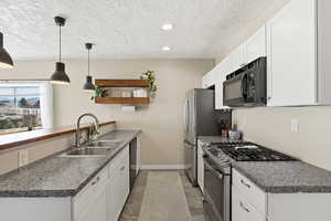 Kitchen featuring white cabinetry, stainless steel appliances, a peninsula, hanging light fixtures, and dark countertops