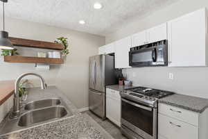 Kitchen with stainless steel appliances, open shelves, white cabinetry, pendant lighting, and a textured ceiling