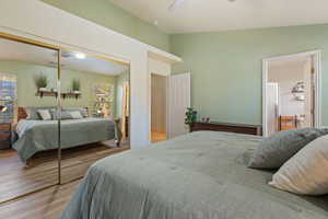 Bedroom with wood finished floors, a closet, ensuite bath, a ceiling fan, and lofted ceiling