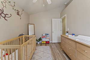 Bedroom with a crib, lofted ceiling, light wood-type flooring, and ceiling fan