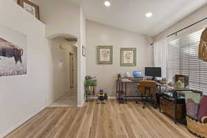 Office area with vaulted ceiling, arched walkways, light wood-style floors, and recessed lighting