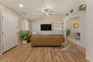 Living area with vaulted ceiling, a ceiling fan, light wood-style flooring, and arched walkways