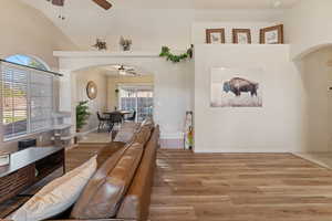 Living area featuring arched walkways, ceiling fan, light wood finished floors, and vaulted ceiling