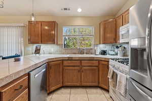 Kitchen with stainless steel appliances, wood finish cabinetry, pendant lighting, light tile patterned floors, and tasteful backsplash