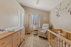 Bedroom with lofted ceiling, a nursery area, light wood-type flooring, ceiling fan, and a closet